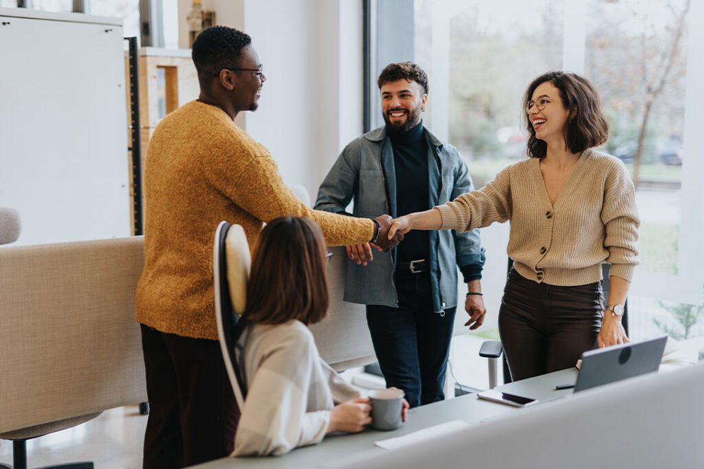 A woman greets a man in an office and shakes his hand